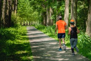 older man and woman running along a wooded trail