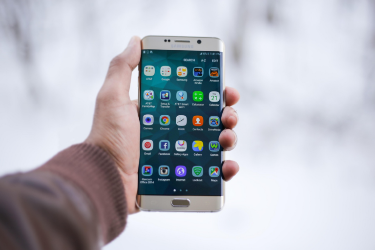 A person holding a smartphone displaying various app icons in a snowy outdoor setting.