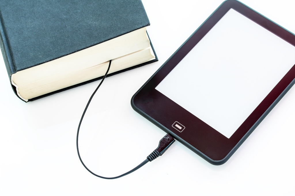 E-reader connected to a book with a charging cable, symbolizing the blend of traditional and digital reading.